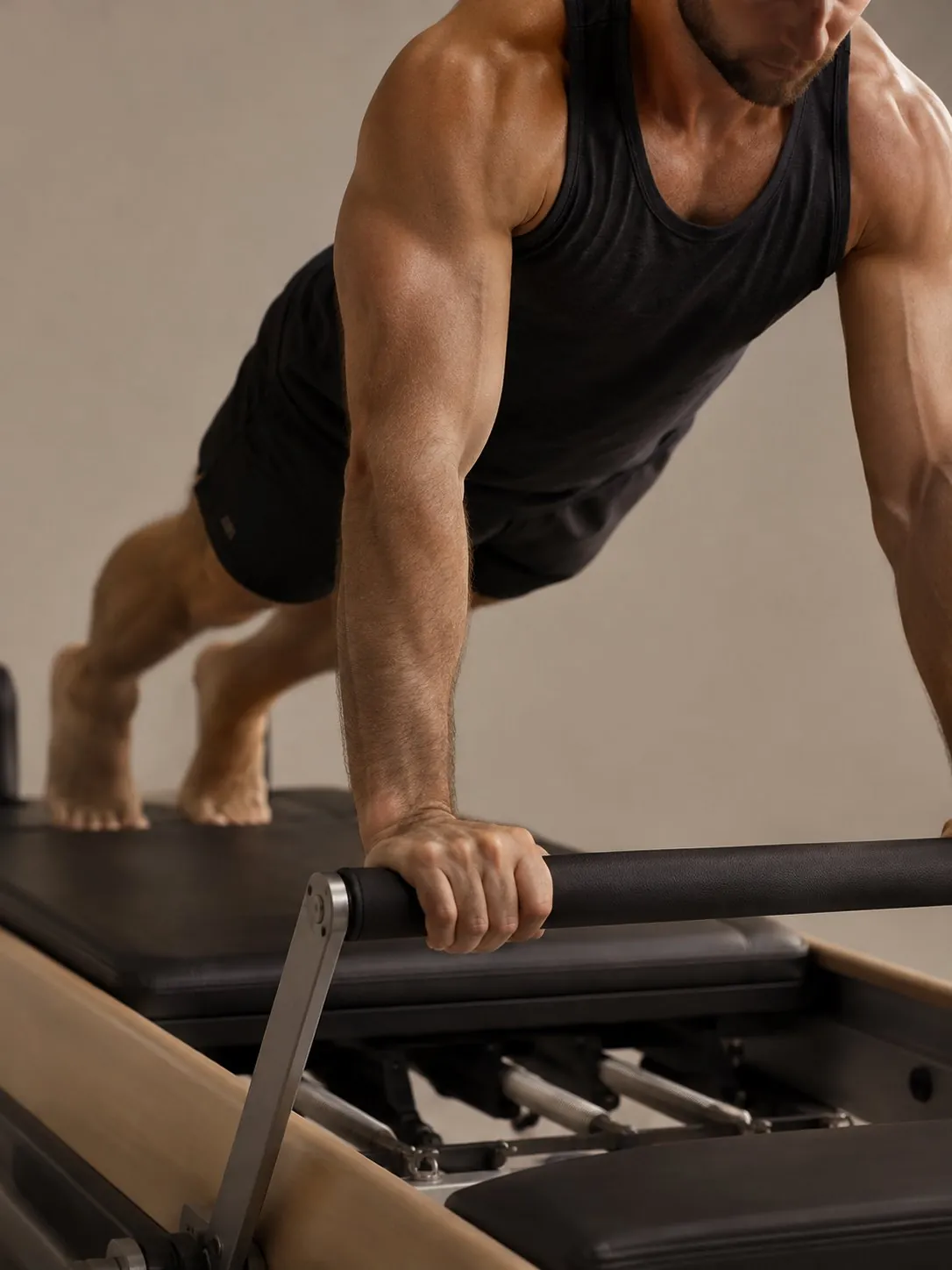 A man in a plank on a reformer, hands on the foot bar